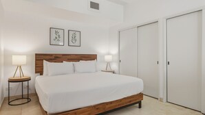 Un dormitorio con cabecera de madera, ropa de cama blanca, dos lámparas de noche y un armario.