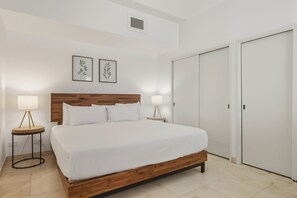 Ein Schlafzimmer mit Holz-Kopfteil, weißer Bettwäsche, zwei Nachttischlampen und einem Kleiderschrank.