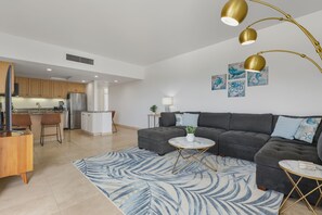 Ein modernes Wohnzimmer mit einem dunkelgrauen Ecksofa, einem runden Couchtisch und einem blau gemusterten Teppich.