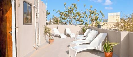 A rooftop terrace with white lounge chairs, potted plants, and a ladder.