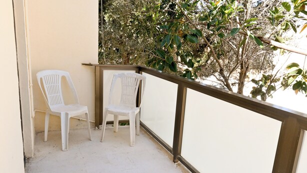 En balkon med to hvide plastikstole og udsigt til træer.