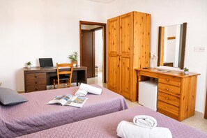 Ein Schlafzimmer mit zwei Betten, einem Schreibtisch, einem Kleiderschrank und einem kleinen Kühlschrank.