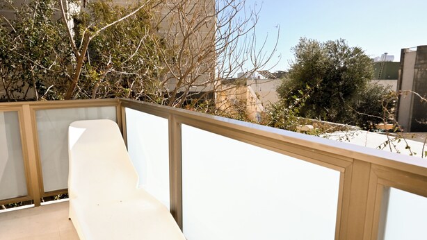 Un balcon avec une chaise blanche, une balustrade en bois et une vue sur des immeubles et des arbres.