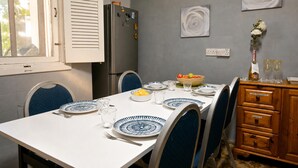 Un coin repas avec une table blanche dressée pour quatre personnes, des chaises bleues, un réfrigérateur et un mur orné de deux œuvres d’art encadrées.