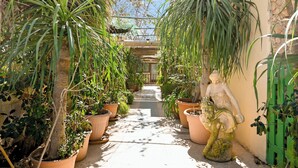 Un étroit sentier bordé de plantes en pot et d’une statue, qui mène à un bâtiment doté d’un toit végétalisé.