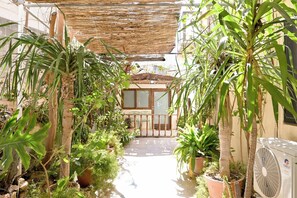 Une cour avec des plantes en pot, un ventilateur et un bâtiment doté d’un balcon.