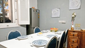 Un coin repas avec une table blanche dressée pour quatre personnes, des chaises bleues, un réfrigérateur et un buffet en bois.