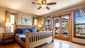 Ein Schlafzimmer mit einem Holzbett, zwei Nachttischen, einem Deckenventilator und einem großen Fenster mit Blick ins Freie.