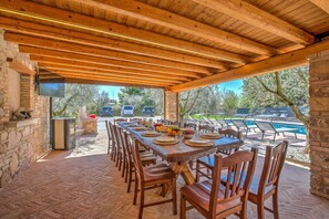 An outdoor dining area with a long wooden table, chairs, and a stone wall. - Residenza Lugana Pool & Garden in Peschiera Apt 4, Peschiera del Garda, Italy (Peschiera del Garda)
