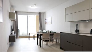 A modern kitchen with a dining area, featuring a large window, a painting, and a built-in stove. - Central Sliema Stay Sea View -steps to Promenade (Sliema)