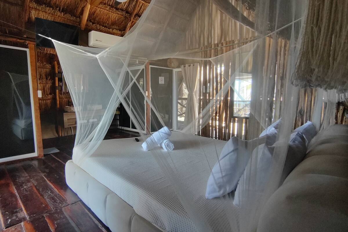 A room with a bed, a mosquito net, and a wooden ceiling.