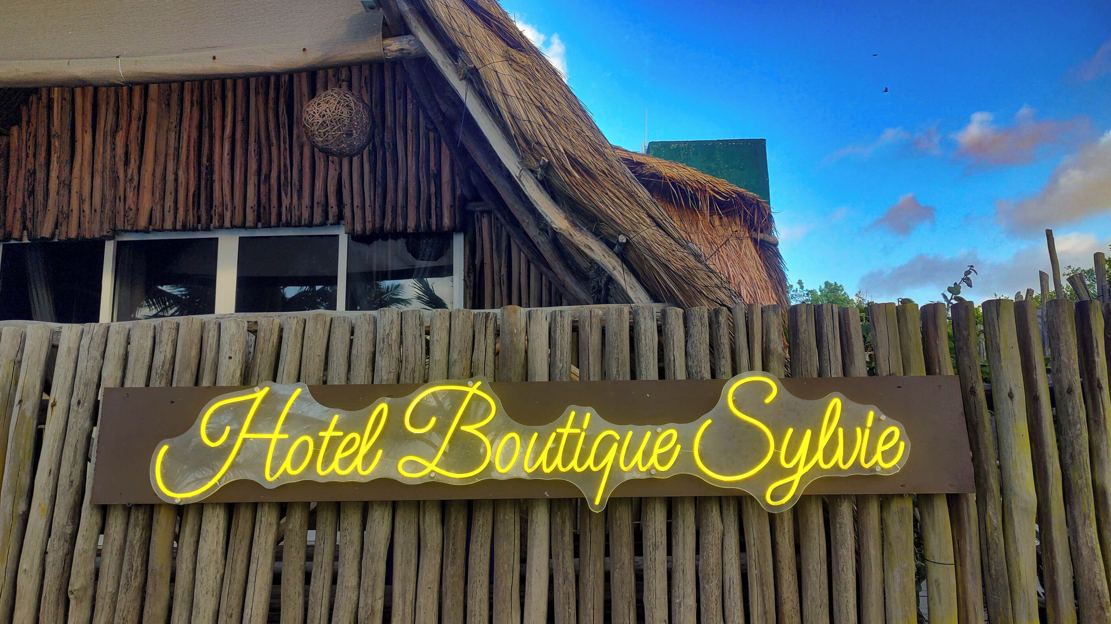 Una valla de madera con un letrero de neón que dice 'Hotel Boutique Sybie'.