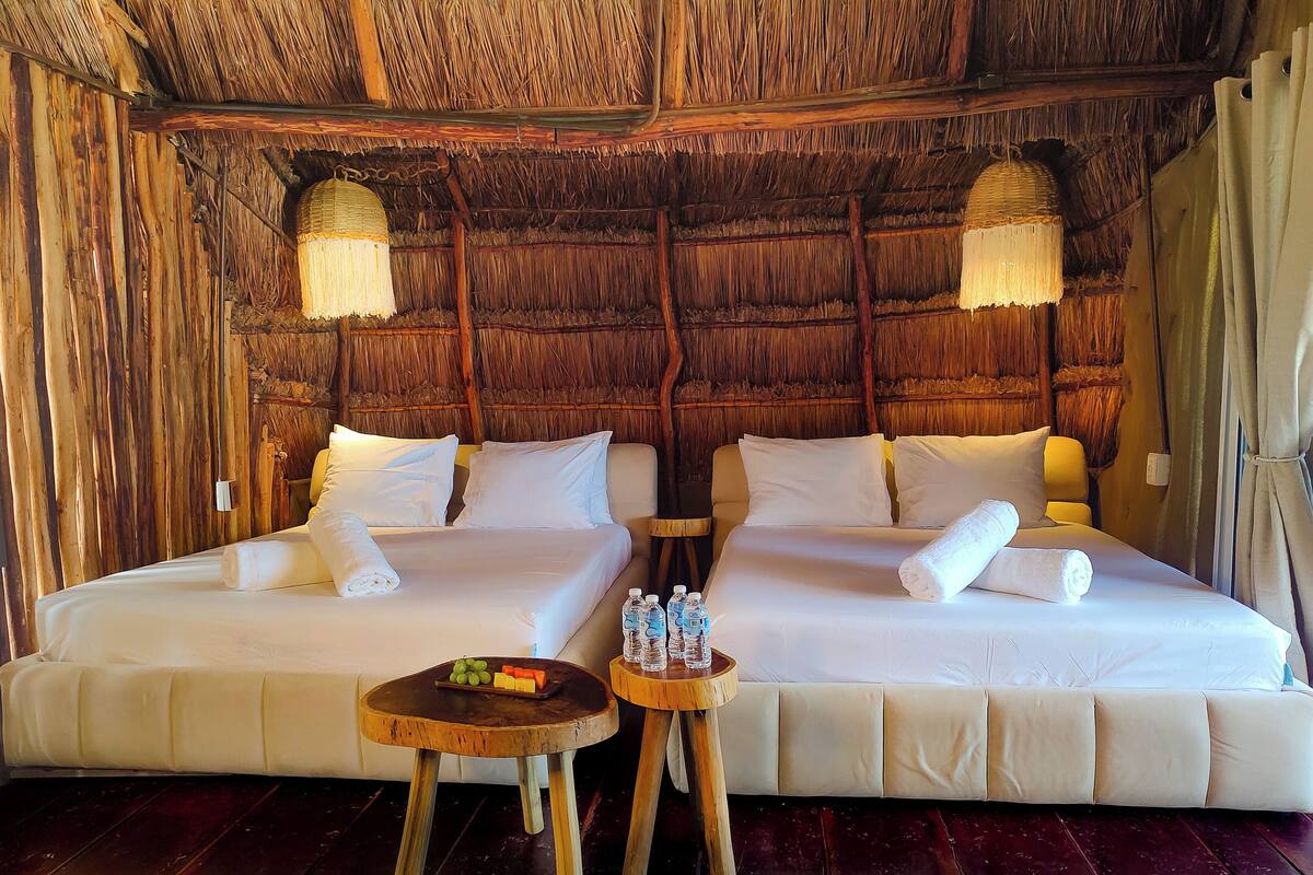 A room with two beds, wooden furniture, and a thatched ceiling.