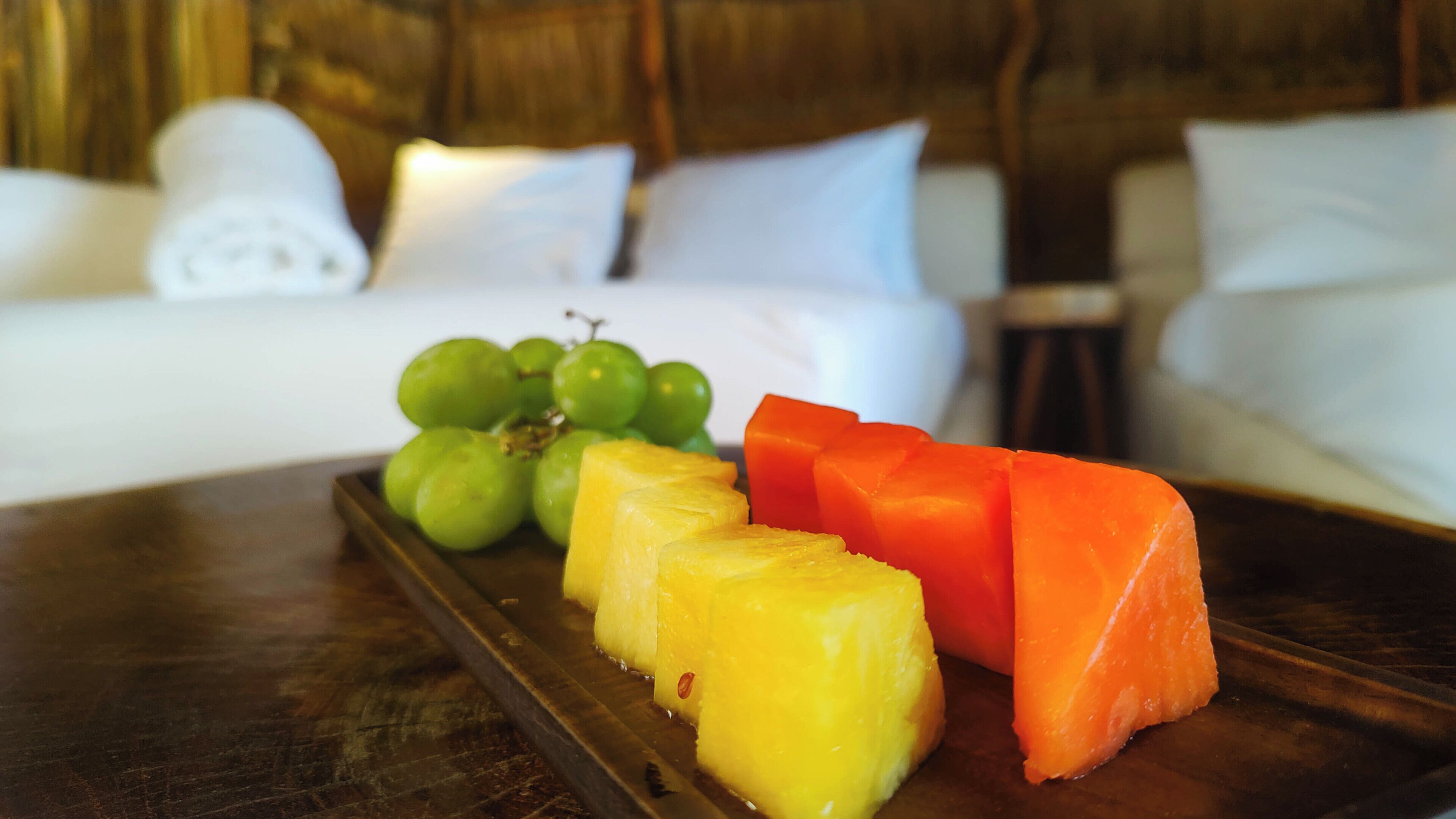 A tray with pineapple slices, watermelon, and grapes on a wooden table in a hotel room.