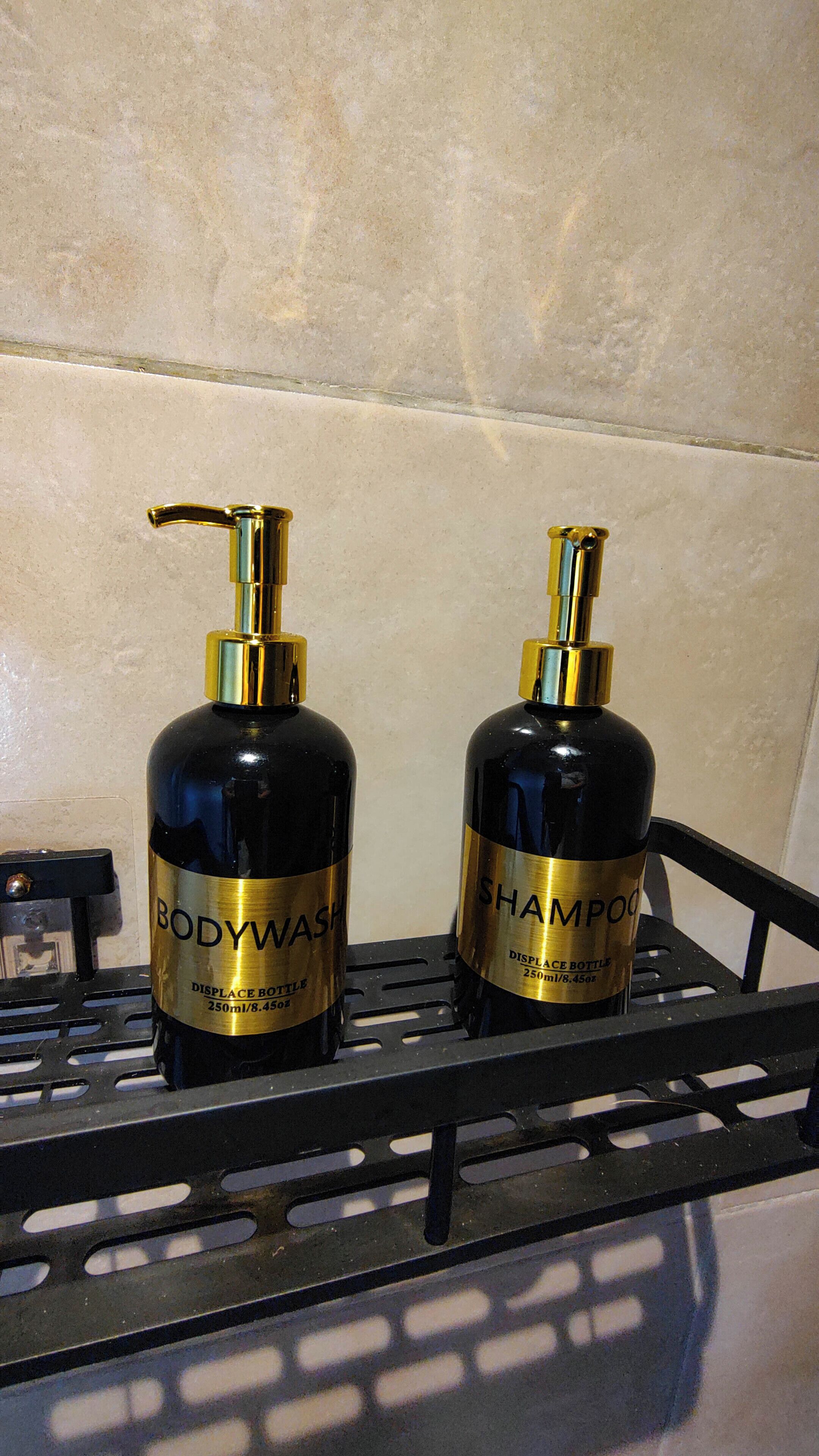 Deux bouteilles de gel douche et de shampoing sur une étagère en métal noir.