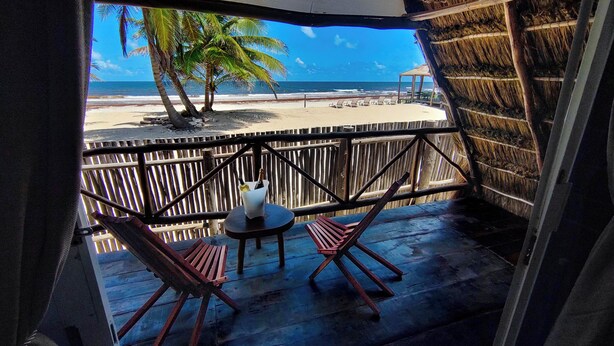 Une terrasse en bois avec deux chaises et une table, donnant sur une plage bordée de palmiers et sur l’océan.