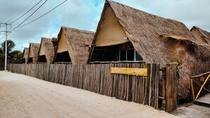 Une rangée de huttes à toits de chaume, protégées par une clôture en bois, avec une enseigne devant, et un ciel dégagé.