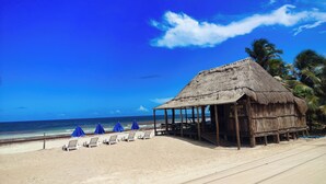 Une cabane de plage avec un toit de chaume, une plage de sable et un ciel bleu dégagé.