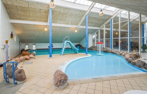 Une piscine intérieure dotée d’un toboggan, d’éléments rocheux et offrant une vue sur l’extérieur grâce à de grandes fenêtres.