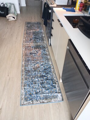 A kitchen with a long blue and beige rug, a white countertop, and a stainless steel dishwasher. - Super Luxury  1-bedroom apartment with amazing view of New Roc city, with extra (New Rochelle)