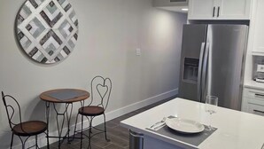 Une cuisine moderne avec des meubles blancs, un réfrigérateur en acier inoxydable, une table de salle à manger ronde avec quatre chaises et un élément décoratif mural.