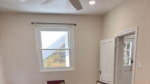 A dining room with a wooden table, four chairs, a ceiling fan, and a window with a view of a mountain. - Stylish City Apt, Walk Everywhere (Pembroke Parish)
