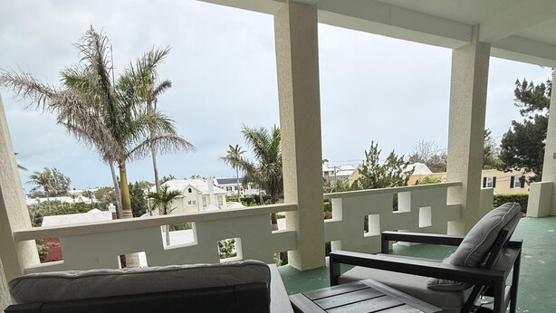 A covered outdoor seating area with a view of palm trees and buildings. - Stylish City Apt, Walk Everywhere (Pembroke Parish)