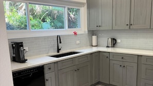 A modern kitchen with grey cabinets, a dishwasher, a coffee maker, and a window with a view of greenery. - Stylish City Apt, Walk Everywhere (Pembroke Parish)