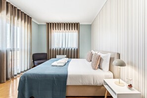 Une chambre d’hôtel avec un lit, une chaise, une table de chevet avec une lampe et une fenêtre avec des rideaux.