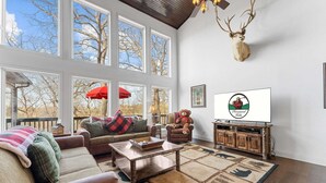 Una sala de estar acogedora con chimenea, ventanas amplias y una cabeza de ciervo montada.
