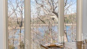 Una mesa de comedor con platos y cubiertos, una ventana con vistas a árboles y una masa de agua.