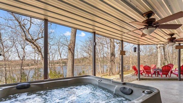Un jacuzzi con vista a árboles y un lago, sillas rojas y un ventilador de techo.