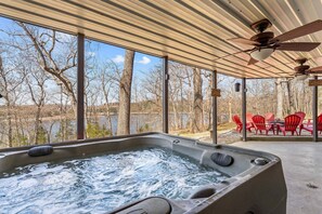 A hot tub with a view of trees and a lake, red chairs, and a ceiling fan.