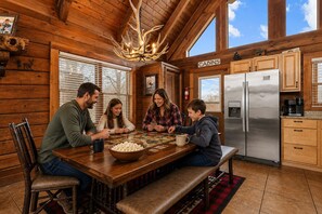 Ein Holzblockhaus-Interieur mit Esstisch, Stühlen, einer Bank, einem Kühlschrank und einem Schild mit der Aufschrift 'CABINS'.