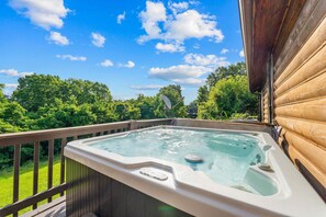 Ein Whirlpool auf einer Holzterrasse mit Blick auf Bäume und einen klaren Himmel.