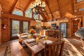 A wooden cabin interior with a dining area, kitchen, and a large chandelier. - Thunder Ridge + Table Rock • Hot Tub • Fenced Yard • Pet Friendly (Ridgedale)