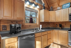 A kitchen with wooden cabinets, a stainless steel dishwasher, a coffee maker, and a sink. - Thunder Ridge + Table Rock • Hot Tub • Fenced Yard • Pet Friendly (Ridgedale)