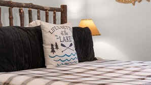 Een bed met een geruite spreidek, een kussen met een ontwerp gebaseerd op een meer, een houten hoofdbord, en een visbordje aan de muur.