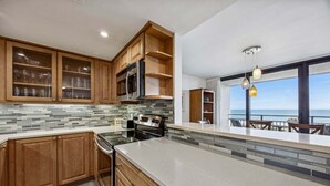 A modern kitchen with wooden cabinets, a stainless steel range, and a large island. - Oceanview 3BR Condo - Beautiful Pool on Amelia Island (Fernandina Beach)