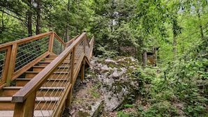 A wooden bridge with a metal railing, surrounded by dense green foliage and rocky terrain. - Mountain Joy: Free Tickets/ Jacuzzi/ Fireplace (Gatlinburg)