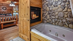 A wooden cabin interior with a stone wall, a fireplace, a wooden bench, and a hot tub. - Mountain Joy: Free Tickets/ Jacuzzi/ Fireplace (Gatlinburg)