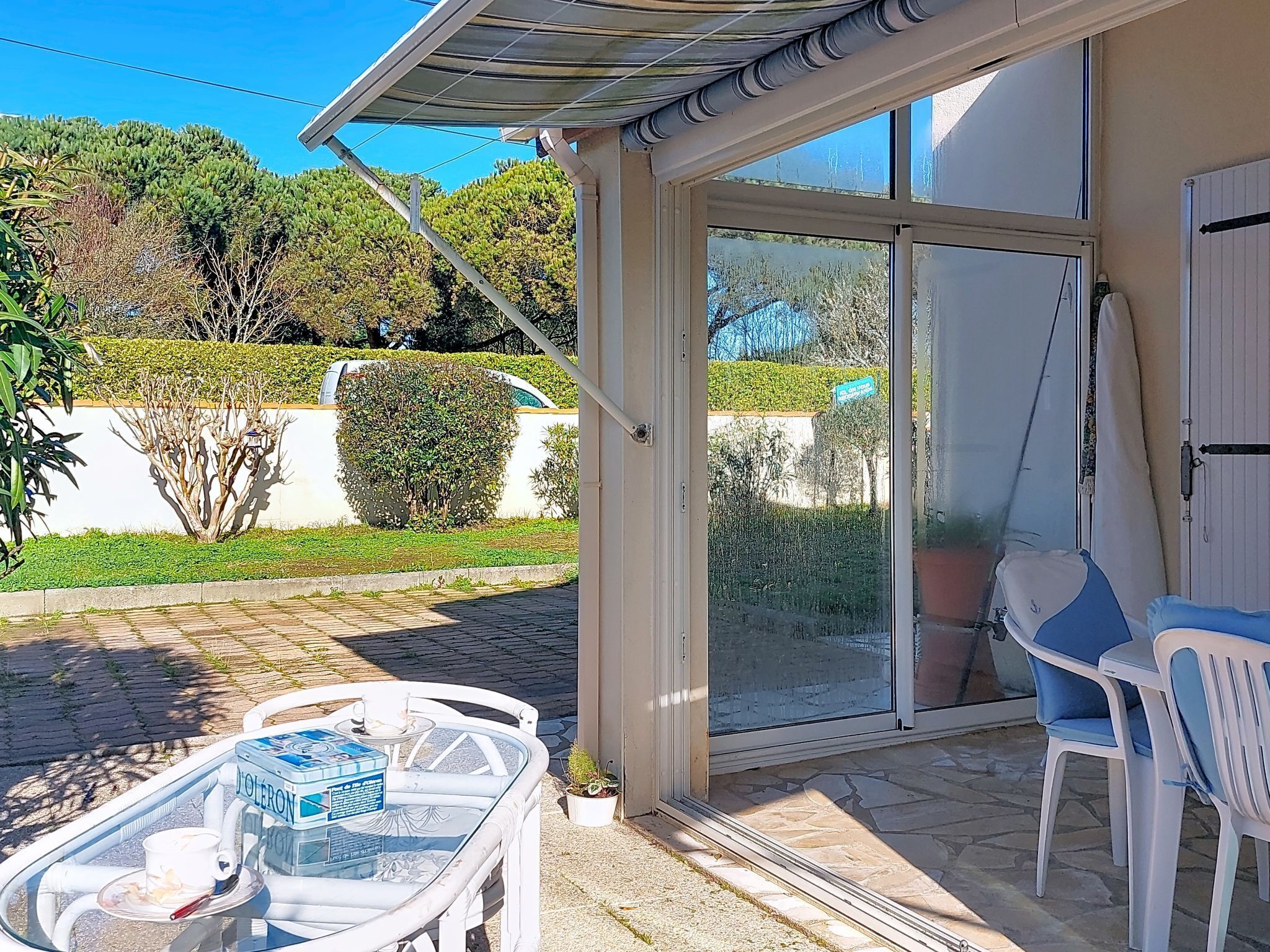 Uma área de pátio com uma mesa de vidro, cadeiras e uma porta de correr que dá para um jardim.