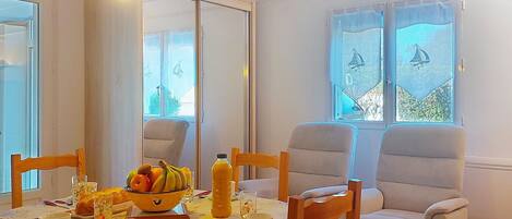 A dining area with a table set for two, featuring a bowl of fruit, a bottle of orange juice, and a floral tablecloth.