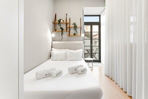 A modern bedroom with a bed, white bedding, a bedside table with a lamp, and a view of the outside balcony. - GuestReady - Charming central Porto retreat (Porto)