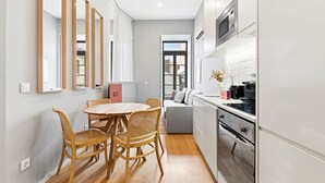 Une cuisine moderne avec des meubles blancs, un four à micro-ondes encastré et une cuisinière. On y trouve également un coin repas avec une table ronde en bois et des chaises en osier.