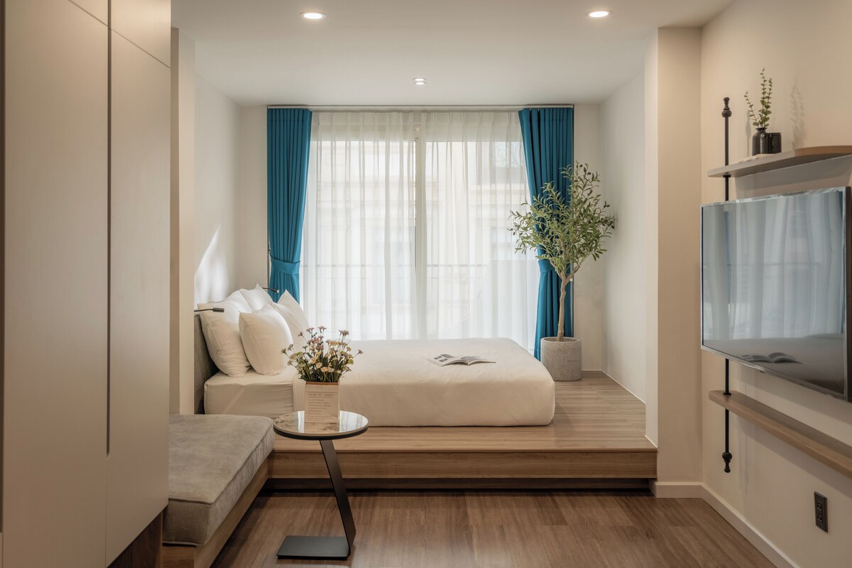 A modern hotel room with a sofa, a small table, a potted plant, and a TV.