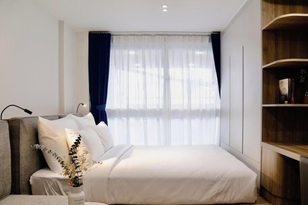 A modern bedroom with a bed, a bedside table, a lamp, and a bookshelf.