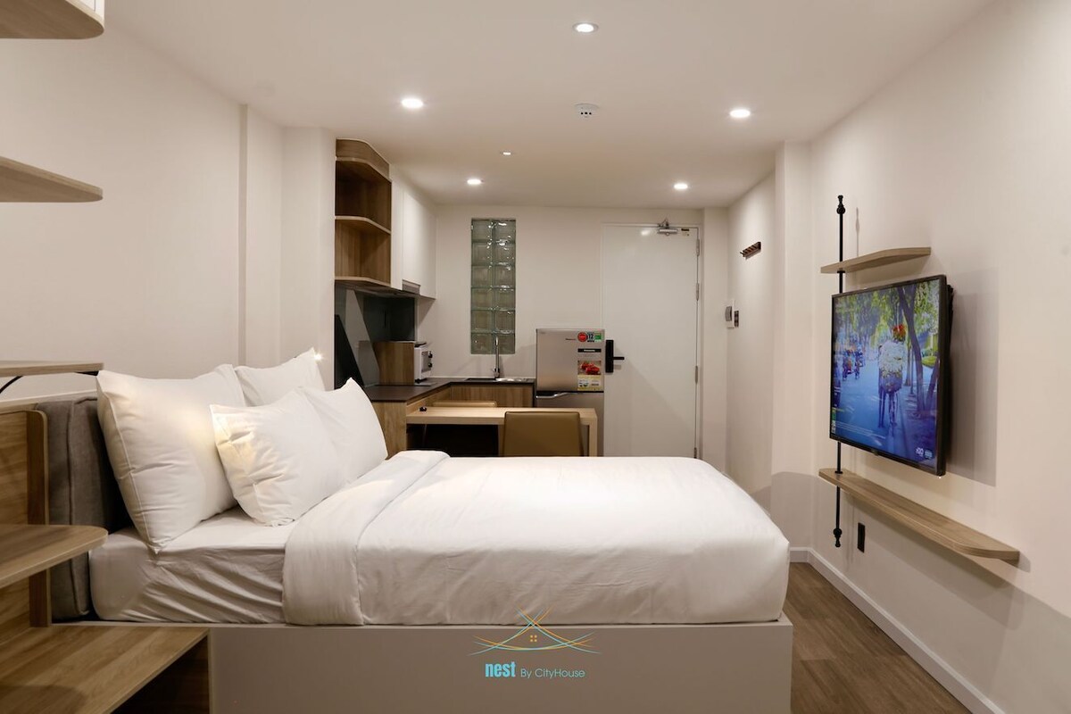 A modern hotel room with a bed, a desk, a television, and a small kitchenette.