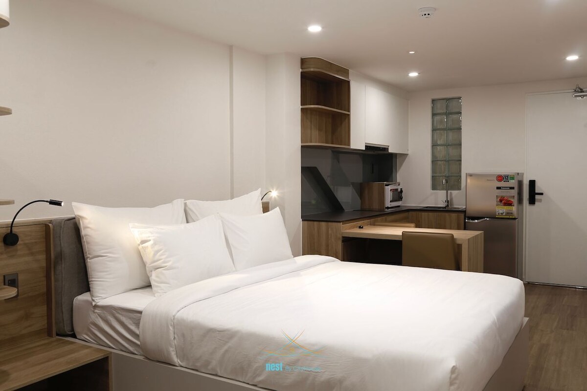 A modern hotel room with a bed, a desk, and a kitchenette.
