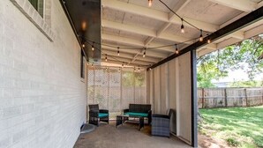 En overdækket terrasse med betongulv, to fletstole med grønne hynder og et lille bord.